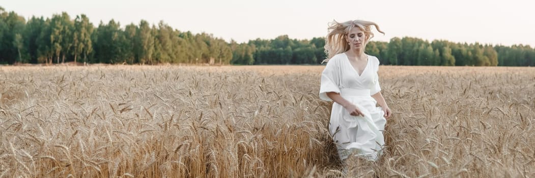 A blonde woman in a long white dress walks in a wheat field. The concept of a wedding and walking in nature.