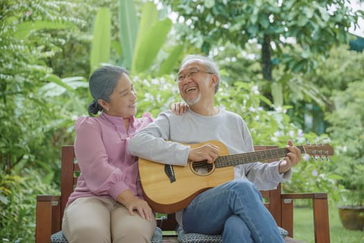 Happy two Asian senior couple elderly man playing the guitar while his wife is singing together at home outdoors, Enjoying lifestyle during retirement life having fun, Activity family health care