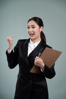 Confident young asian businesswoman in formal suit holding clipboard with hand gesture indicating promotion or advertising with surprised facial expression on isolated background. Enthusiastic