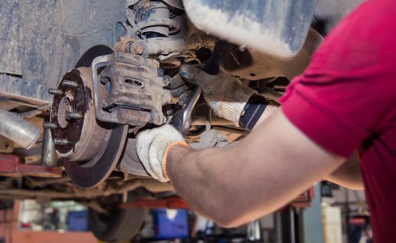 Male hands fasten or unscrew the wheel support of the old car with a wrench. In the garage, a man changes parts on a vehicle. Small business concept, car repair and maintenance service. UHD 4K.