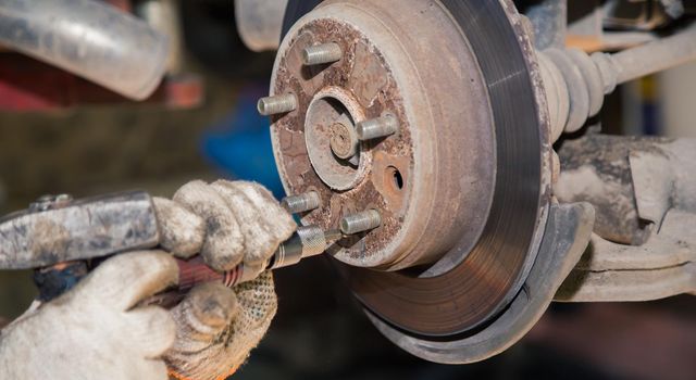 Gloved hands remove the rear rusted wheel hub. In the garage, a man changes parts on a vehicle. Small business concept, car repair and maintenance service. UHD 4K.