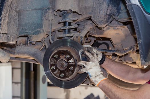 Gloved male hands install or remove the brake caliper of an old car. In the garage, a man changes parts on a vehicle. Small business concept, car repair and maintenance service. UHD 4K.