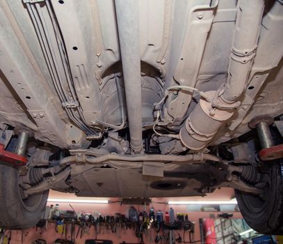 Bottom view of the underbody and wheels of an old car on a lift. In the garage, a man changes parts on a vehicle. Small business concept, car repair and maintenance service. UHD 4K.