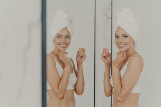 Pretty young woman reflected in mirror doing morning routine holds toothbrush while brushing teeth in bathroom at home, effective treatment for healthy white tooth. Personal oral care concept