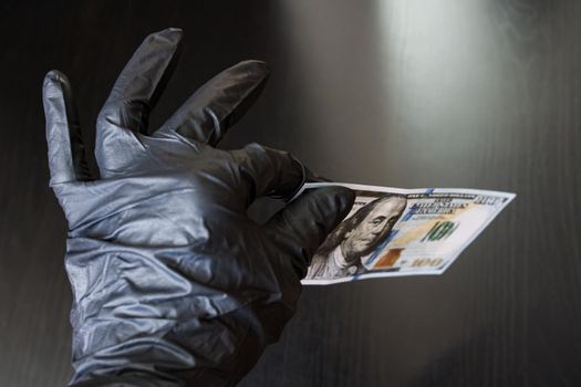 A hand in a black glove holds a dollar