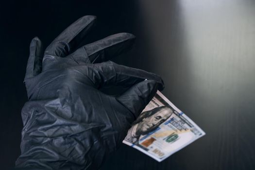 A hand in a black glove holds a dollar