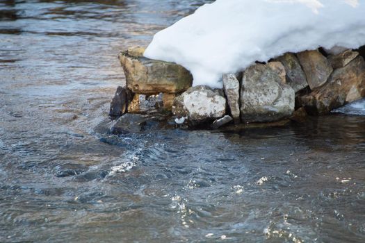 Winter landscape of a river with seething water and snow-capped rocky banks. A stormy stream of water with white foaming waves and ripples.