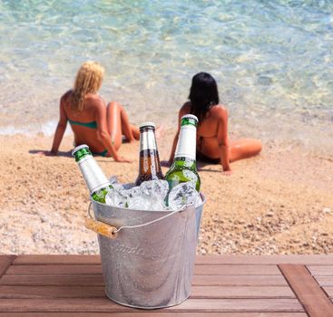 Three unopened bottles of beer inside ice bucket on beach background