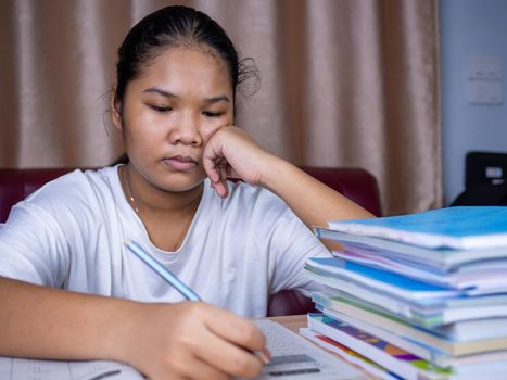 girl doing homework on a wooden table and there was a pile of books next to it The background is a red sofa and cream curtains.