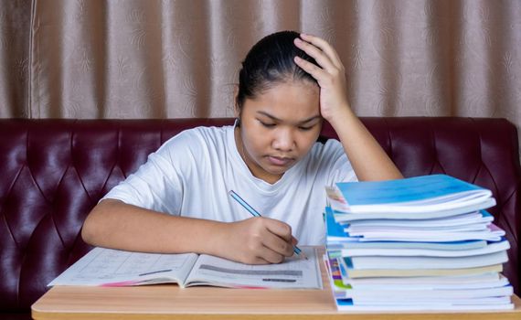 girl doing homework on a wooden table and there was a pile of books next to it The background is a red sofa and cream curtains.