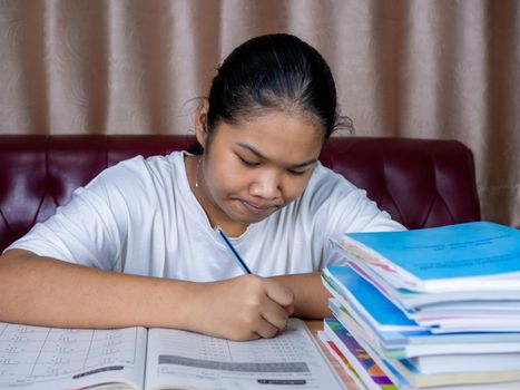 girl doing homework on a wooden table and there was a pile of books next to it The background is a red sofa and cream curtains.