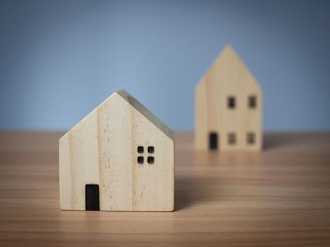 Two wooden model houses placed on a wooden table. with a light gray background