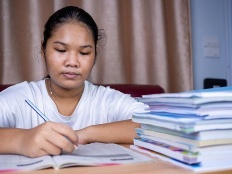 girl doing homework on a wooden table and there was a pile of books next to it The background is a red sofa and cream curtains.