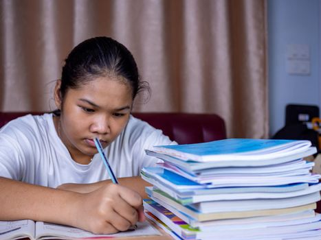 girl doing homework on a wooden table and there was a pile of books next to it The background is a red sofa and cream curtains.