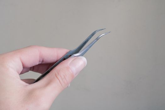 Tweezers in hand on a gray background close up