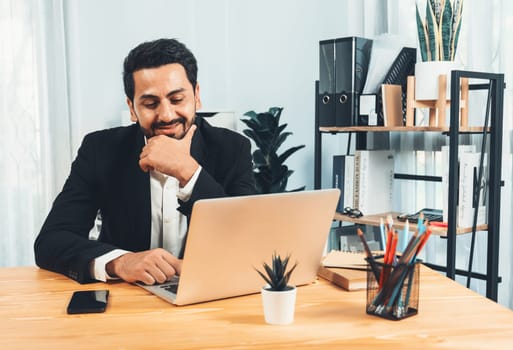 Modern professional businessman at modern office desk using laptop to work and write notes. Diligent office worker working on computer notebook in his office work space. fervent