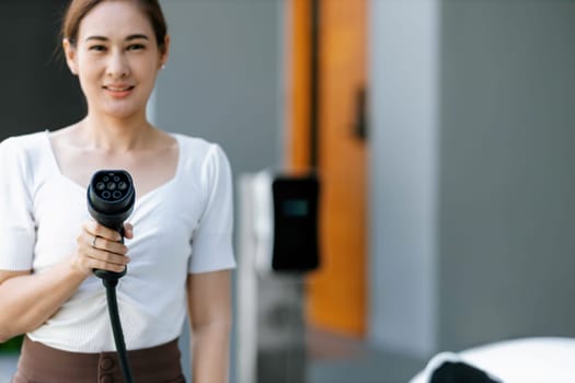 Closeup man holding and pointing an EV plug for electric vehicle at camera as progressive idea of alternative sustainable clean and green energy for environmental and ecology concern.