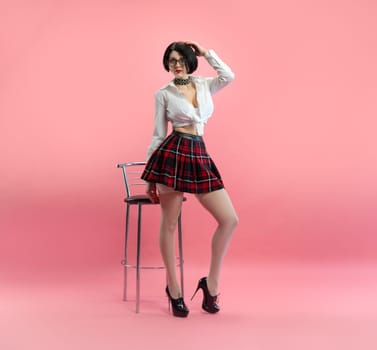 sexy girl with glasses in an erotic schoolgirl costume from a sex shop and white stockings on a pink background copy paste
