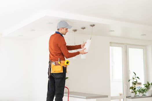 Electrician in uniform repairing ceiling lamp indoors.