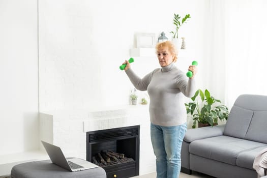 Training At Home. Sporty senior woman doing yoga plank while watching online tutorial on laptop, exercising in living room, free space, panorama.