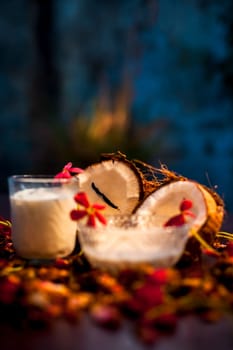 Coconut face mask consisting of coconut milk and yogurt for flawless skin and to moisturize it. Shot of raw coconut cut coconut, milk, and yogurt with some flowers spread on the brown wooden surface.