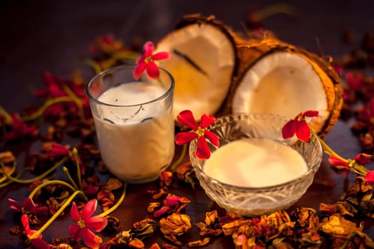 Coconut face mask consisting of coconut milk and yogurt for flawless skin and to moisturize it. Shot of raw coconut cut coconut, milk, and yogurt with some flowers spread on the brown wooden surface.