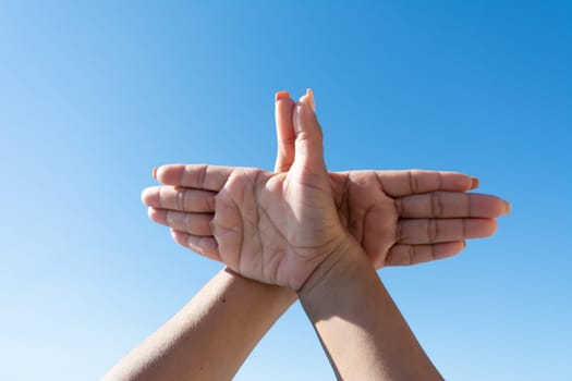 woman's hands making dove sign with her hands against blue sky,
