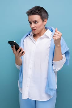 excited young woman with short haircut using smartphone on blue background.