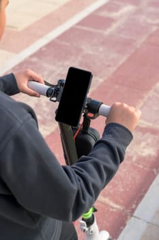 young man riding an electric skateboard outdoors, looking at route on smartphone map application, sustainable transport concept, zero CO2 emission green energy