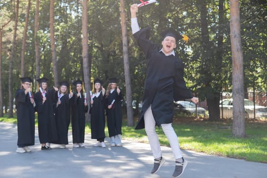 Happy young caucasian man celebrating graduation. Crowd of students graduates outdoors