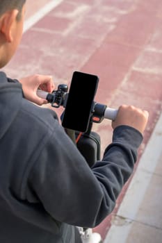 young man riding an electric scooter outdoors, looking at route on smartphone map application, sustainable transport concept, zero CO2 emission green energy