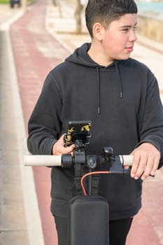 young teenager with a sideways glance riding an electric sscooter and using a smartphone application E-Mobility urban leisure concept