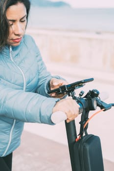side view of Beautiful latin woman riding her motorized scooter in the city, activating smart phone app, mobility concept sustainable transport, zero CO2 emissions