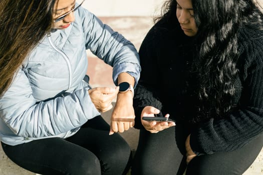 two beautiful long hair latin women synchronizing data on smart phone and smart watch, shopping on the net, internet shopping concept