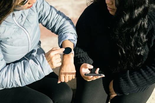 Two young beautiful female friends with smart devices texting and chatting having fun on social media, smart phone r and smart watch smart technology concept