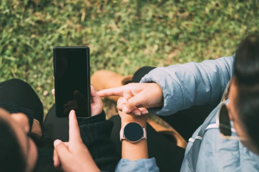 Cropped hands of a woman with a smart watch, pointing to a smartphone, concept of technology, social networking, with two people indicating something on the smartphone.