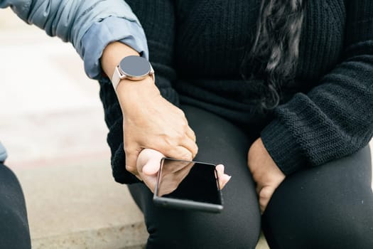 Two Spanish-Latino women with smartphones and smartwatches, selective focus on the clipped hands. technological concept of communication and freedom