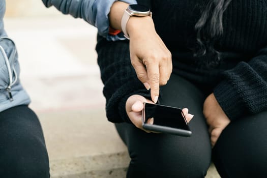 two women dressed in black clothes, using smart electronic devices, smart phone and smart watch, sharing information from social networks and online shops.