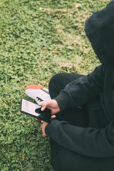 young man sitting on the ground in the park, completely immersed in his smartphone. he appears to be in his own little world, scrolling through his phone's contents.