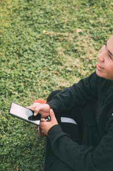 cheerful teenager of Latino descent smiles as he looks at his smartphone screen. The boy's relaxed posture and cheerful expression convey a sense of contentment. Background blurred to focus attention on the boy and his phone.