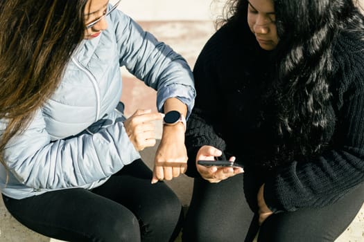 Two young beautiful female friends with smart devices texting and chatting having fun on social media, smart phone r and smart watch smart technology concept