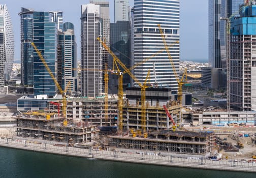 Cranes surround the construction of new tower for apartments along canal in Business Bay Dubai UAE