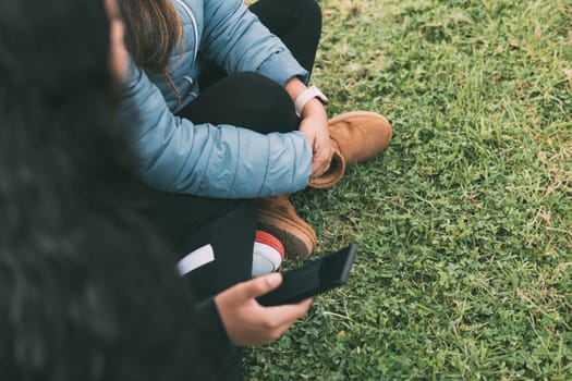 group of three Hispanic friends enjoying a beautiful day in the park, while bonding over their shared love of technology. The photo is taken from a side view, so their faces are not visible, but we can see them sitting on the ground, with one of the young men holding a smartphone, which they all seem to be looking at. social aspects of technology use in modern society, as well as the importance of spending time outdoors and sharing experiences with friends. comcept friendship, leisure time, technology use, and multiculturalism.