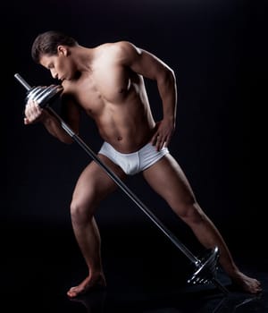 Brawny young man posing kissing barbell, isolated on black