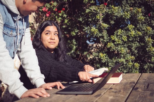 two young latinos study outside of high school, with laptop and books do scientific work, collaborative concept