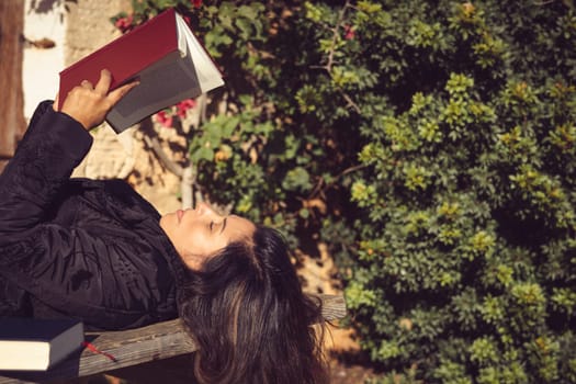 woman holds an open book in the garden, concentrating on reading attentively.
