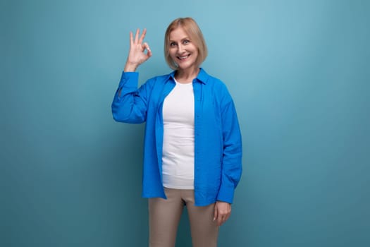 joyful smiling 50s middle aged woman in a blue shirt on a blue background with copy space.