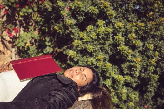 close-up of latin woman sleeping with a book under her head in the garden on a wooden table