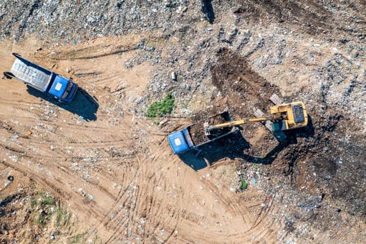 Aerial top view of excavator and dump trucks working at the construction site