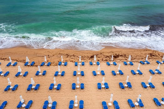 Aerial view of a fantastic beach with, blue lounge chairs, umbrellas, and turquoise sea.